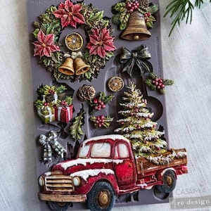 May include: A grey silicone decor mould titled Country Christmas Delivery featuring various holiday-themed shapes including a poinsettia wreath with bells, a bell with holly, a bow, a pinecone, gift boxes, a Christmas tree, and a red pickup truck.