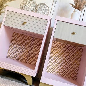 May include: Two pink bedside tables with light wood drawer fronts and gold hardware. The interior features a gold geometric pattern. The base and legs are gold. The text "THE GRANDSON'S BRUSH" is at the bottom.