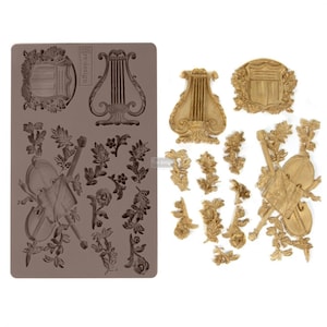 May include: A silicone mold and casted resin embellishments. The mold is brown and features a lyre, violin, and floral designs. The casted pieces are gold and include a lyre, shield, violin, and various floral sprigs. Ideal for crafting and decorative projects.