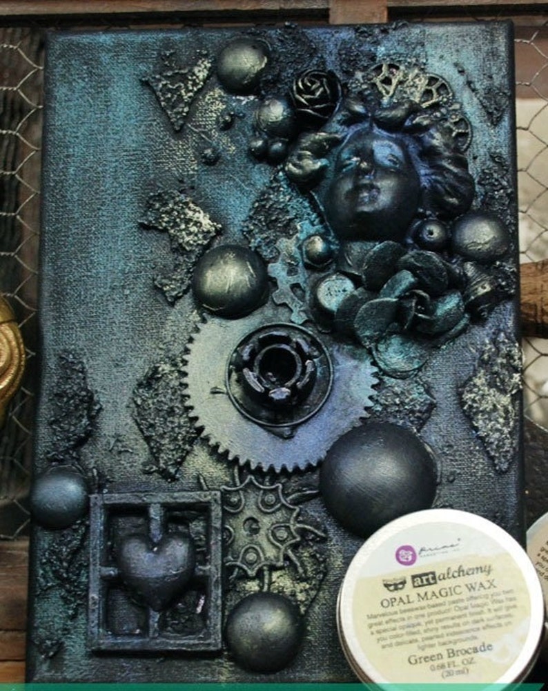 May include: A mixed media art piece on canvas with a blue and green color scheme. The piece features a variety of textures, including metal gears, beads, and a sculpted face. The piece is finished with a layer of green wax, which gives it a shimmering effect. The wax jar is labeled "Green Brocade" and "Opal Magic Wax".