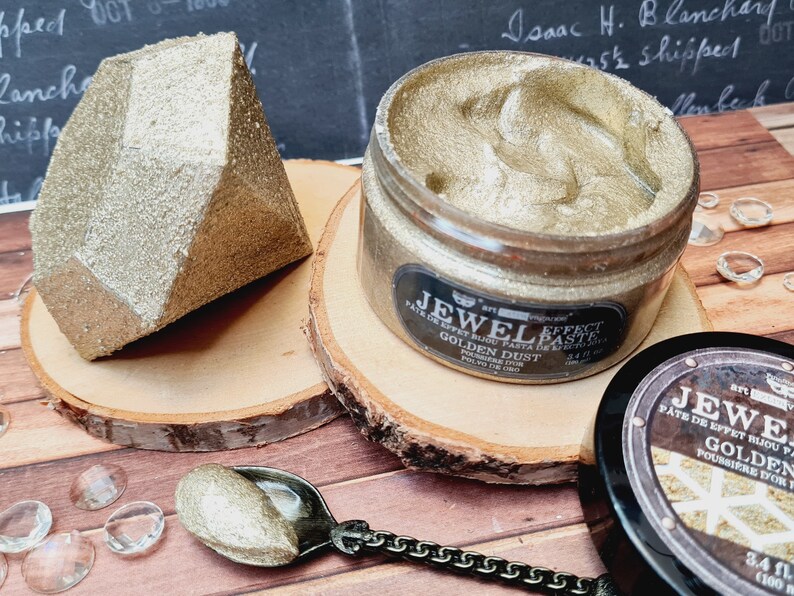 Puede incluir: Un tarro de pasta de efecto Jewel Effect en color Golden Dust, con una textura dorada met&aacute;lica. La etiqueta dice Jewel Effect Paste Golden Dust 100 ml. Al lado hay una forma geom&eacute;trica dorada facetada y una cuchara peque&ntilde;a con la pasta.