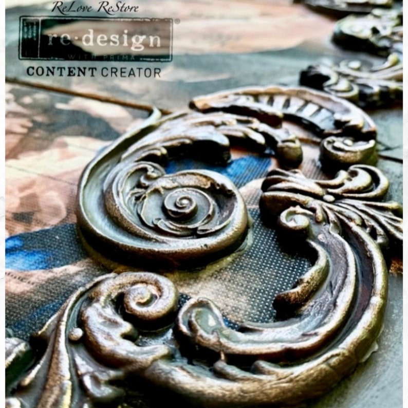 May include: Close-up of ornate, bronze-coloured decorative moulding with scroll and leaf designs. The moulding is set against a patterned background with the text "re-design" and "CONTENT CREATOR".