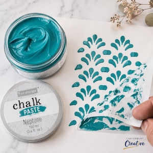 May include: A jar of teal chalk paste labeled Neptune 100 ml 3.4 fl. oz. with a matching lid and a stencil being lifted to reveal a repeating teal teardrop pattern on a white surface. The paste has a thick, smooth, and creamy consistency.