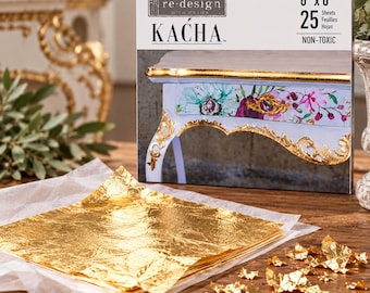 May include: A pack of 25 gold leaf sheets measuring 6 inches by 6 inches, labeled re-design with prima KAĆA. The packaging features an image of a light blue table with floral patterns and gold trim. A stack of gold leaf rests on white tissue paper.
