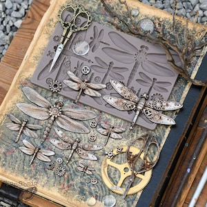 May include: An assortment of steampunk-style dragonfly embellishments and gears in various sizes. The image includes a silicone mold, decorative scissors, and finished dragonflies with intricate mechanical details. The color palette is primarily metallic silver and bronze.