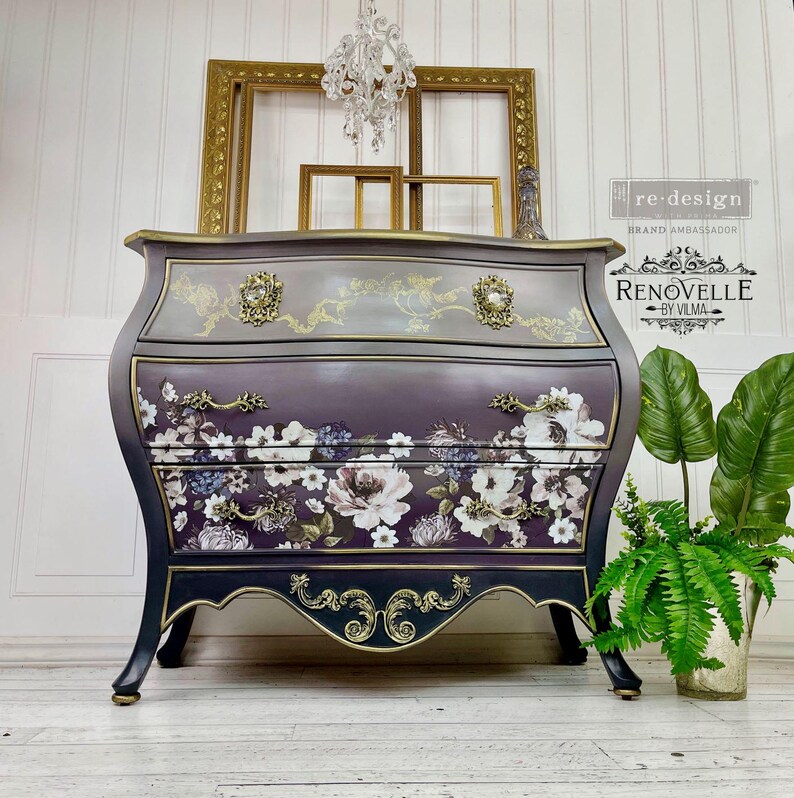May include: A three-drawer chest of drawers with a curved front, painted in shades of purple, grey, and black. The drawers feature a floral pattern and gold hardware. The top and base have gold accents.