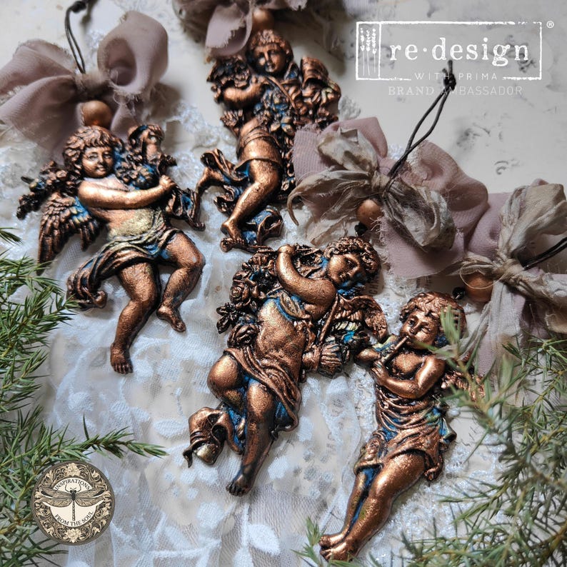 May include: Ornate bronze-colored cherub figurines with blue accents. The cherubs are in various poses, some holding flowers or playing instruments. The image includes the text "re-design with Prima Brand Ambassador".