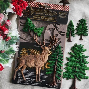 May include: A silicone decor mould set titled Stag of the Highlands featuring a brown stag figure and several green pine tree shapes. The packaging includes text detailing the product name and usage instructions on a dark background.