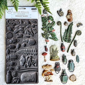 May include: A gray silicone mold with various botanical and insect designs, including leaves, beetles, and ferns. The package reads "DECOR MOULDS MIDNIGHT MUSES." Several painted resin embellishments of insects, mushrooms, and plants are also displayed.