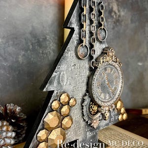 May include: A decorative Christmas tree-shaped ornament with a distressed silver finish. It features a vintage clock, gold geometric accents, and hanging chains. The text "Re-design MC DECO STUDIO Petites" is visible.