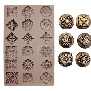 May include: A silicone mold with various ornate, floral, and geometric designs, alongside six finished decorative embellishments. The mold is a muted brown color, and the embellishments are metallic gold and bronze.