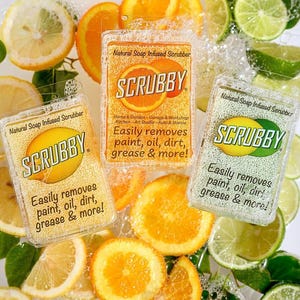 May include: Three natural soap-infused scrubbers with the brand name "SCRUBBY" are surrounded by citrus fruits. The scrubbers are in clear packaging and feature the text "Easily removes paint, oil, dirt, grease & more!"