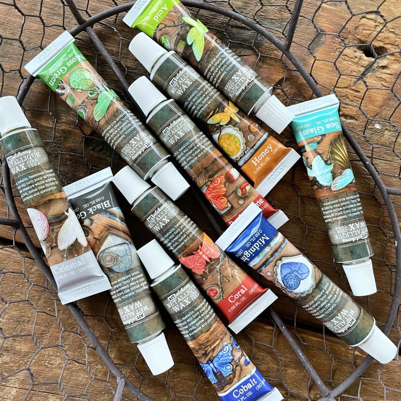 May include: Assortment of 12 metallic wax tubes in various colors, including cobalt, coral, midnight, sea glass, moss green, honey, black gold, celestial, and pixie. Each tube features a unique design and the text "Metallic Wax" on the label.