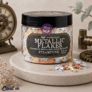May include: A clear plastic jar with a black lid containing metallic flakes in gold, silver, and copper colors. The label reads Metallic Flakes Steampunk 5 fl. oz. (150 ml). Several loose flakes are scattered on the surface in front of the jar.