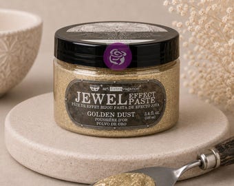 May include: A round plastic jar of Prima Art Extravagance Jewel Effect Paste in Golden Dust. The label displays the product name and a volume of 3.4 fl. oz. A metal palette knife with a wooden handle holds a dollop of the gold glittery paste.
