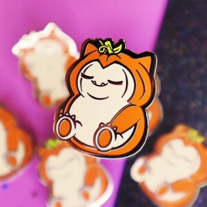 Op de afbeelding: Een set van vijf oranje en witte emaille pinnen met een cartoonfiguur dat verkleed is als een pompoen. Het personage heeft een glimlach met gesloten ogen en draagt een pompoenkostuum met een groene steel erop.