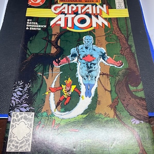 May include: Captain Atom comic book cover featuring a blue superhero with a red star on his chest flying through a green jungle with a red and yellow superhero in the foreground. The cover text reads "Captain Atom" and "Millennium Week 4".