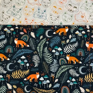 May include: Two fabric patterns are shown. The top fabric has a repeating pattern of fox faces in orange, blue, and brown on a cream background. The bottom fabric has a dark blue background with foxes, mushrooms, rainbows, ferns, and moons.