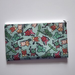 May include: A rectangular pouch with a white zipper. The pouch is light blue and covered in a repeating pattern of cartoon-like creatures, flags, and leaves in various colors including red, green, and orange.