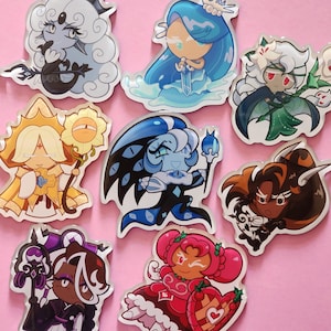 May include: A collection of nine colorful cartoon character stickers. Each sticker features a unique design with various colors, including blue, yellow, pink, and brown. The stickers are on a pink background, showcasing the diverse character designs.