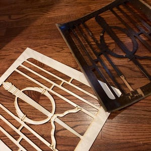 Puede incluir: Dos plantillas de madera, una de color marrón claro y otra de color marrón oscuro, con intrincados diseños geométricos. Las plantillas están dispuestas sobre un suelo de madera.