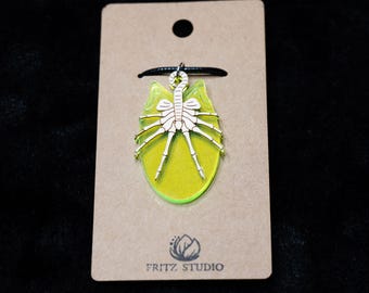 May include: A yellow and white alien creature pendant necklace on a brown card with the text "FRITZ STUDIO".