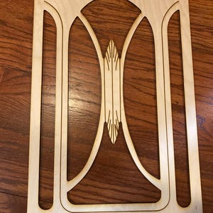 Puede incluir: Un recorte de madera con un diseño decorativo que presenta una forma arqueada con un centro puntiagudo. El recorte está hecho de madera de color claro y tiene un acabado liso.