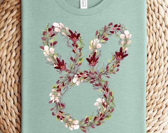 May include: A teal blue t-shirt with a floral design in the shape of the number eight. The design features burgundy and white flowers.