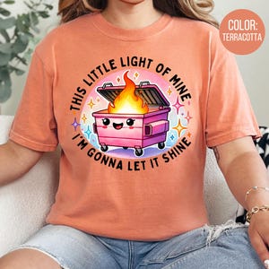 May include: A terracotta t-shirt featuring a pink bin with a fire inside and the text "This little light of mine I'm gonna let it shine".