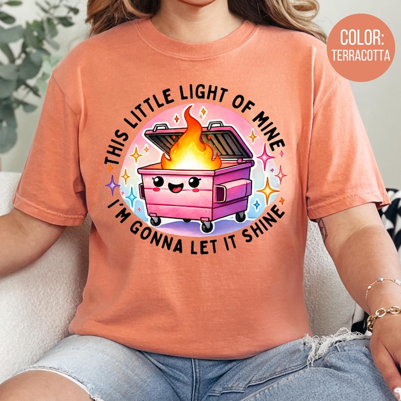 May include: A terracotta t-shirt featuring a pink bin with a fire inside and the text "This little light of mine I'm gonna let it shine".