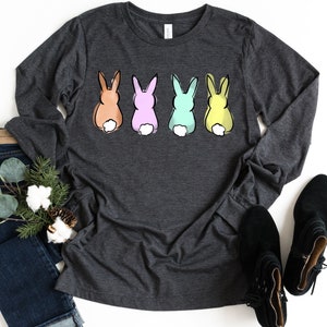 May include: A long-sleeved charcoal grey t-shirt with a graphic of four pastel colored bunnies. The bunnies are facing away from the viewer and have white tails.