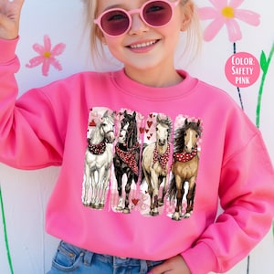 May include: A bright pink sweatshirt with a graphic of four horses wearing bandanas and surrounded by hearts. The horses are white, black, and brown. The text "COLOR: SAFETY PINK" is in a pink circle.