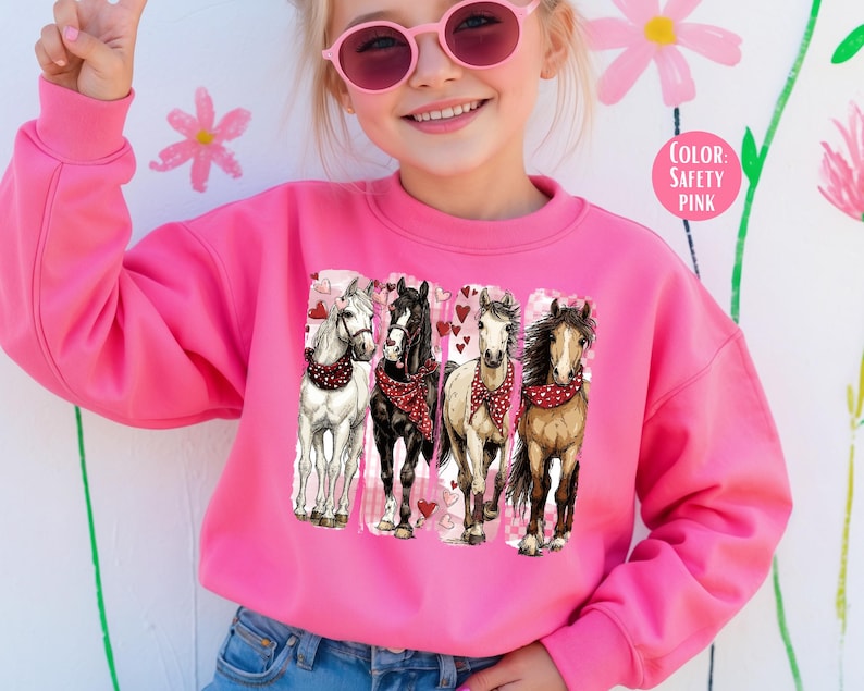 May include: A bright pink sweatshirt with a graphic of four horses wearing bandanas and surrounded by hearts. The horses are white, black, and brown. The text "COLOR: SAFETY PINK" is in a pink circle.