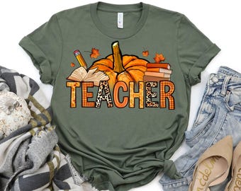 May include: A green t-shirt with a pumpkin, books, and a pencil design. The text "TEACHER" is written in a colorful, patterned font.