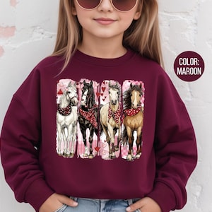 May include: Maroon sweatshirt with a graphic of four horses wearing red bandanas and surrounded by hearts. The horses are white, black, tan, and brown. The sweatshirt is worn by a person with sunglasses.