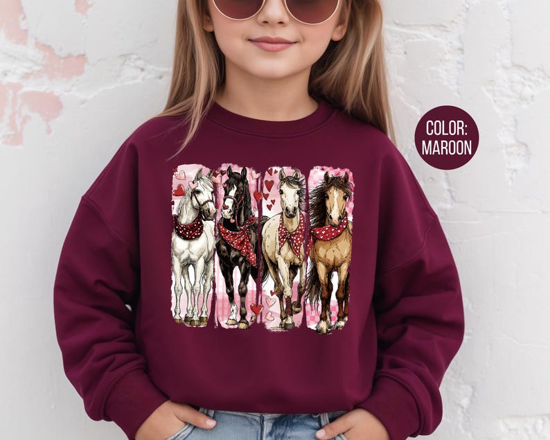 May include: Maroon sweatshirt with a graphic of four horses wearing red bandanas and surrounded by hearts. The horses are white, black, tan, and brown. The sweatshirt is worn by a person with sunglasses.