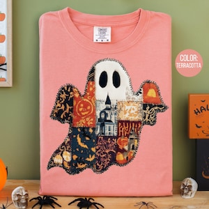 May include: Terracotta-colored t-shirt featuring a patchwork ghost design. The ghost is composed of various patterned fabric pieces, including pumpkins and haunted houses. The shirt has a crew neck and a Comfort Colors tag.