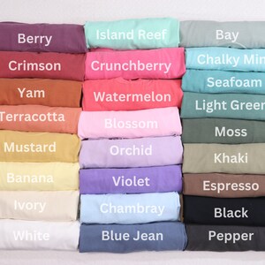 May include: A colour chart of 24 fabric swatches, each folded in half. The swatches are arranged in three columns of eight swatches each. The swatches are labelled with names such as "Berry", "Island Reef", "Bay", "Crimson", "Crunchberry", "Chalky Mint", "Seafoam", "Yam", "Watermelon", "Light Green", "Terracotta", "Blossom", "Moss", "Mustard", "Orchid", "Khaki", "Banana", "Violet", "Espresso", "Ivory", "Chambray", "Black", "White", "Blue Jean", and "Pepper".