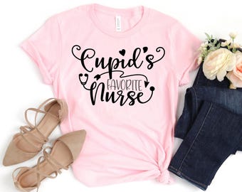 May include: Pink t-shirt with the text "Cupid's Favorite Nurse" in black lettering.