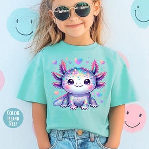 May include: A young person wearing a turquoise blue t-shirt with a colorful cartoon axolotl graphic. The axolotl is surrounded by pink hearts. The text "Color Island Reef" is visible in the lower left corner of the image.