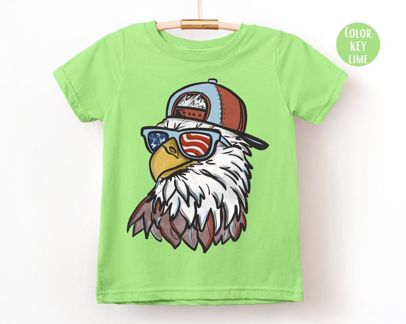 May include: A lime green t-shirt featuring a cartoon eagle wearing a red, white, and blue baseball cap and sunglasses. The sunglasses have a patriotic American flag design. The eagle has white feathers and a yellow beak.