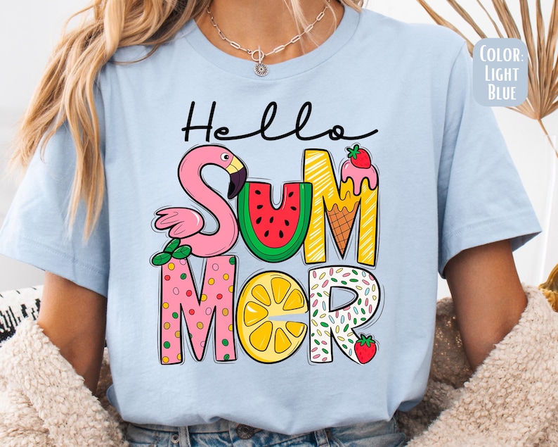 May include: Light blue t-shirt with the text "Hello Summer" in colorful letters. The letters are decorated with a flamingo, watermelon, ice cream cone, lemon, and sprinkles.