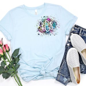 May include: A light blue t-shirt with a rainbow splatter design and a monogram in the center. The monogram is in a leopard print pattern.