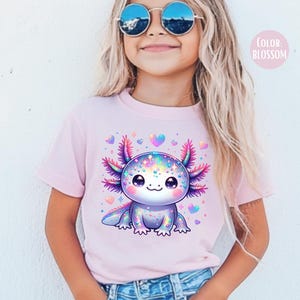May include: A pink t-shirt with a colorful cartoon axolotl wearing a sparkly outfit. The axolotl is surrounded by pink hearts. The text "COLOR: BLOSSOM" is in the top right corner of the image.