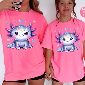 May include: Two pink t-shirts with a cartoon axolotl wearing a sparkly, iridescent design. The axolotl is surrounded by small pink hearts. The text "COLOR: NEON PINK" is in the top right corner of the image.