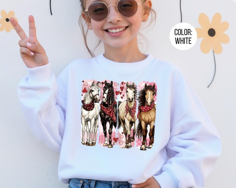 May include: White sweatshirt with a graphic of four horses wearing red bandanas, set against a pink heart backdrop. The horses are depicted in white, black, and brown. The text "COLOR: WHITE" is in a white circle.