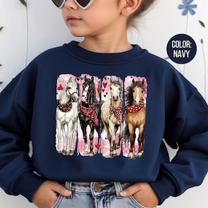 May include: Navy blue sweatshirt with a graphic of four horses wearing red bandanas, set against a pink heart backdrop. The sweatshirt has a crew neck and long sleeves. The colour is navy.