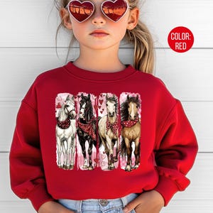 May include: A red sweatshirt with a graphic of four horses, each with a different coat colour and wearing a red bandana. The horses are set against a white background with pink hearts. The text "COLOR: RED" is in a red circle.