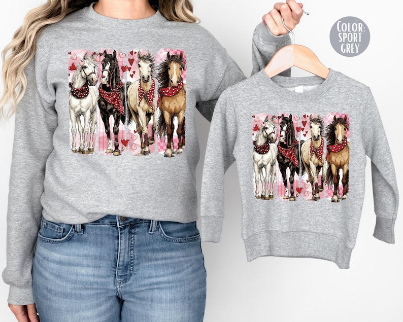 May include: Sport grey sweatshirt featuring a graphic of four horses with red bandanas, set against a pink and white background with hearts. The sweatshirt is shown in adult and child sizes.