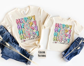 Peut inclure: Deux t-shirts de couleur naturelle avec un motif coloré d'un lapin et le texte "Joyeuses Pâques".